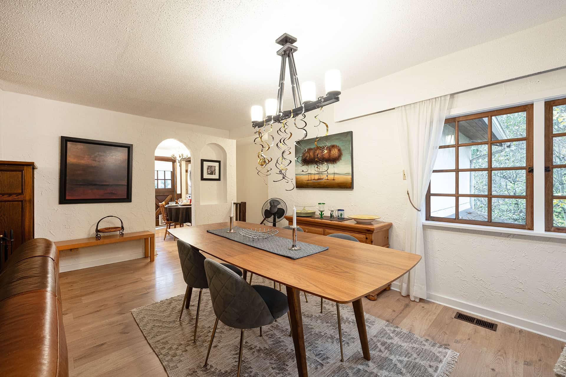 Warm wooden dining room with contemporary chandelier, textured white walls, large window, and cozy decor, showcasing Orca Realty's elegant properties in Victoria BC.