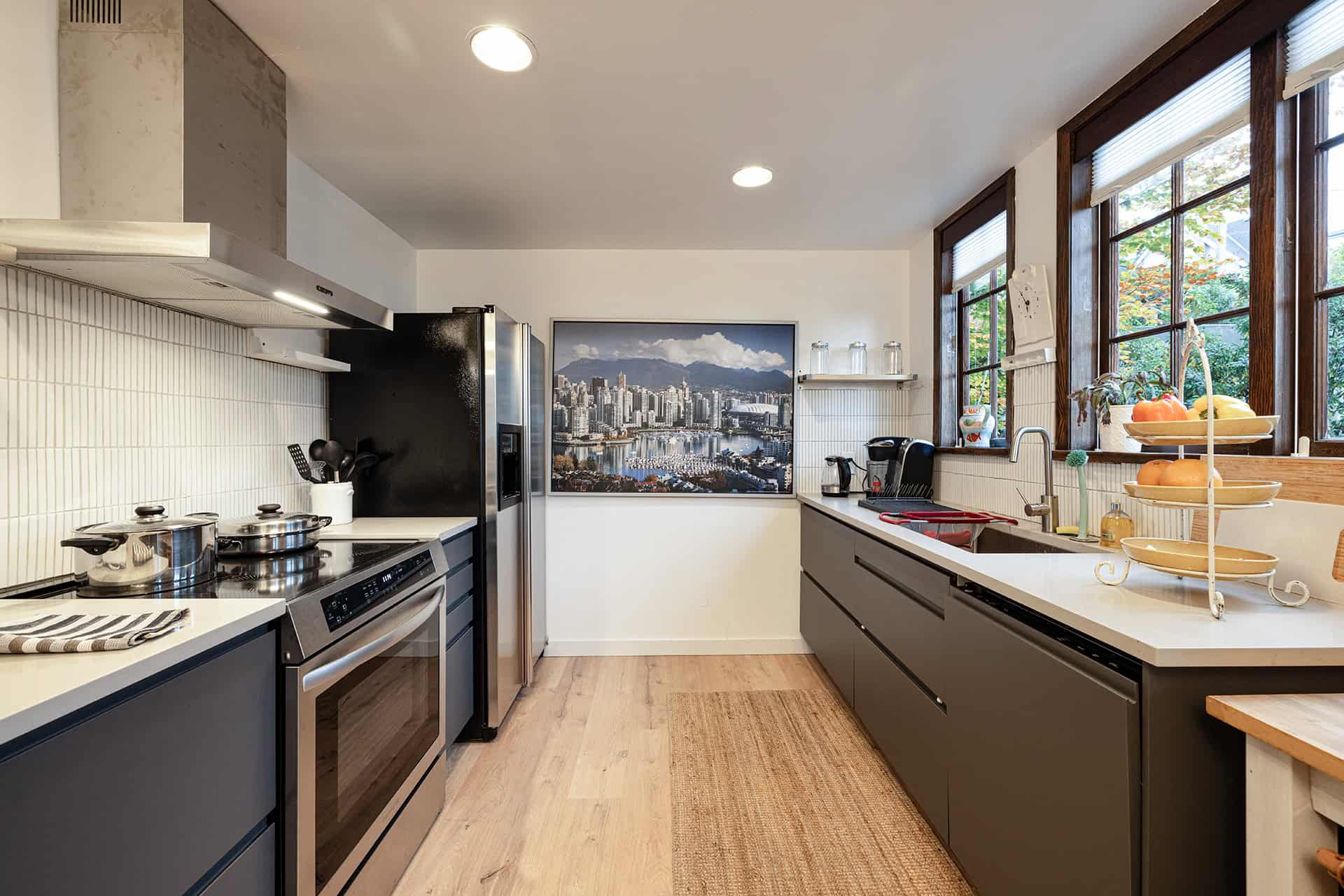 Modern Vancouver kitchen with stainless steel appliances and large windows overlooking a lush garden, featuring sleek grey cabinetry, wood accents, and plenty of natural light for a stylish and functional space.