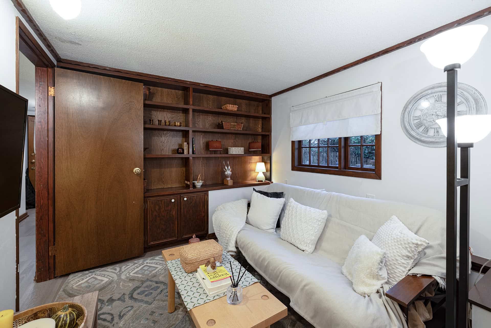 Cozy living room with white sofa and wooden bookshelf, featuring large windows and warm lighting, perfect for relaxing and home comfort, showcased by Orca Realty Inc.