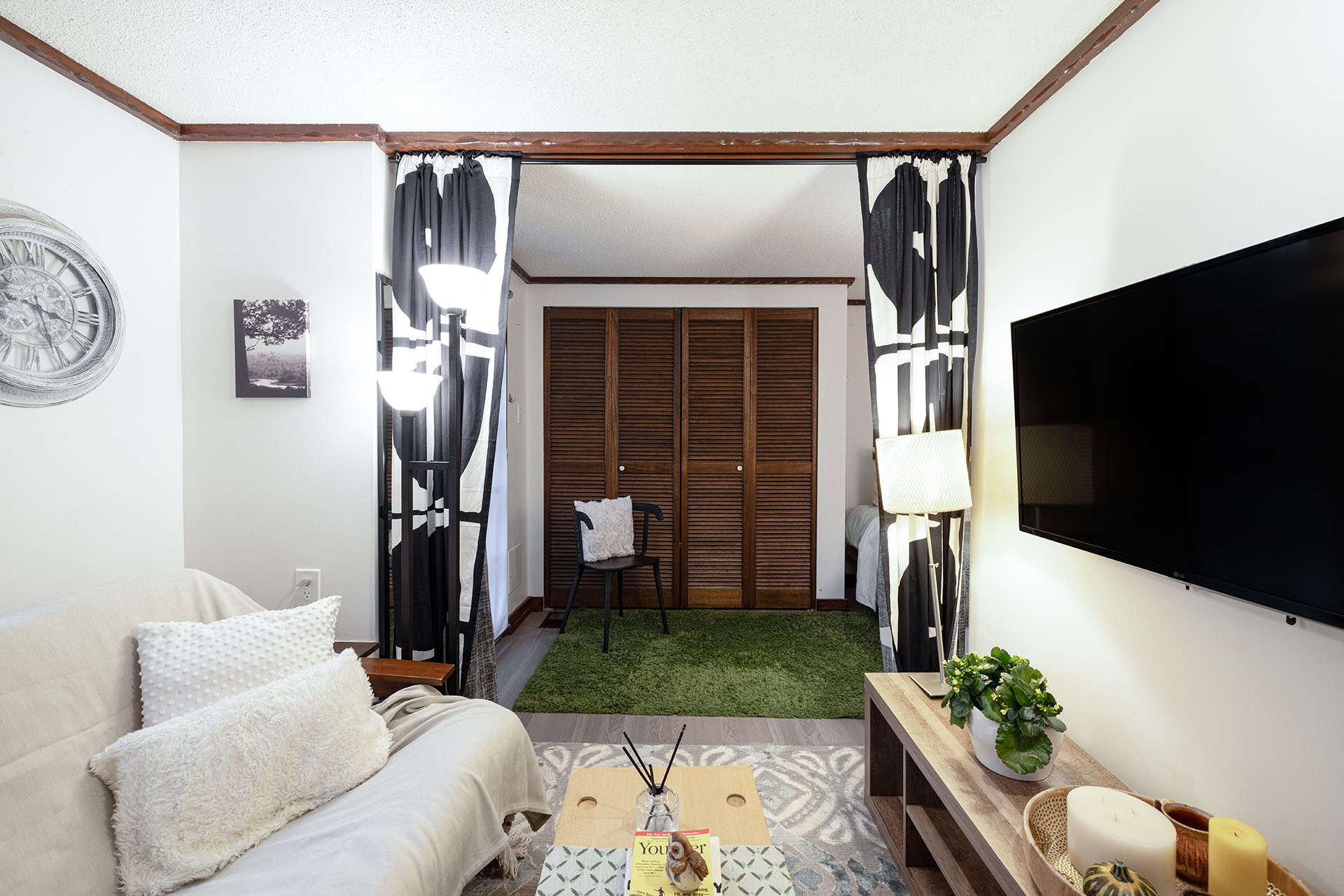 Cozy living room with white sofa, decorative pillows, and wooden furnishings, featuring a flat-screen TV, black and white patterned curtains, and natural light, ideal for Vancouver real estate and home staging.