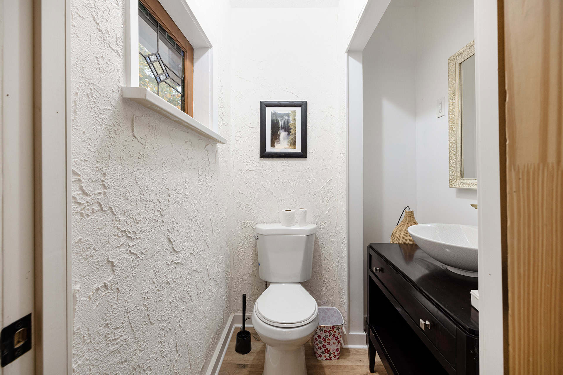 Cozy small bathroom with textured white walls, a modern toilet, decorative framed artwork, and a stylish black vanity with a vessel sink in a home listed by Orca Realty Inc.