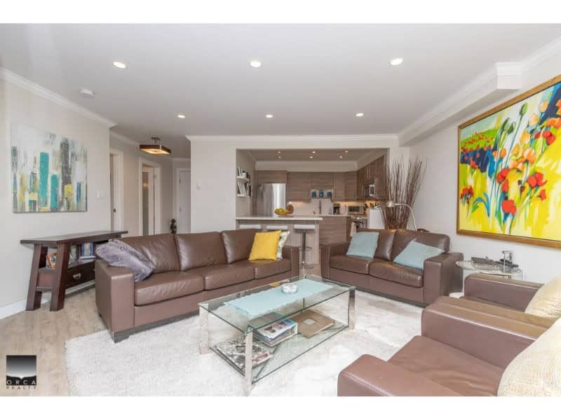 Modern living room interior with brown leather sofas, colorful artwork, and open kitchen - ideal for Vancouver real estate listings.