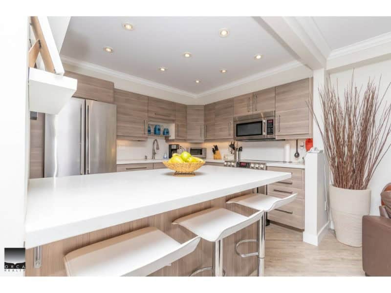 Modern kitchen with stainless steel appliances and minimalist design, featuring a large island and ample storage, ideal for Vancouver Island real estate and homebuyers.