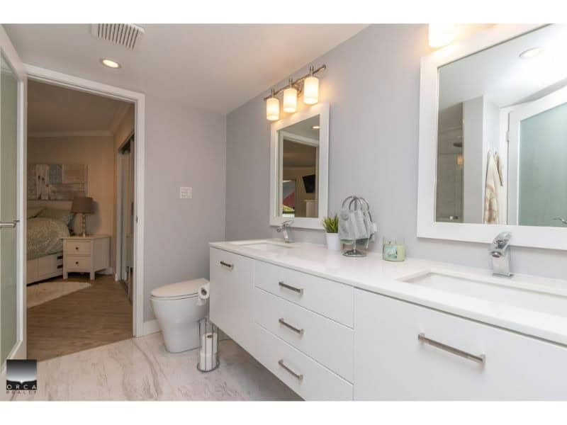 Modern white bathroom vanity with double sinks and large mirror in a bright, airy bathroom at Orca Realty Inc. in Victoria, BC. Features sleek cabinetry, contemporary lighting, and fresh decor.