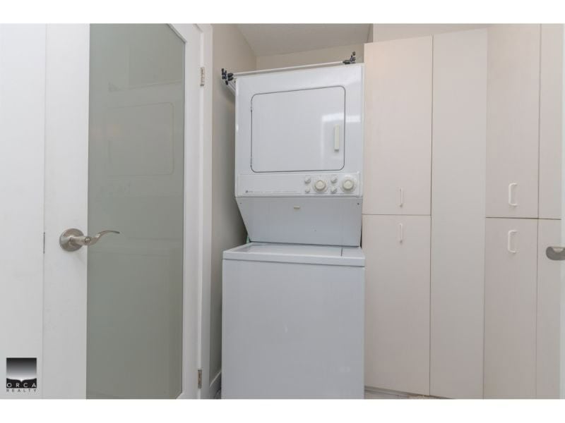 Stacked washer and dryer in laundry room with white cabinets behind, modern home appliances, compact laundry area.