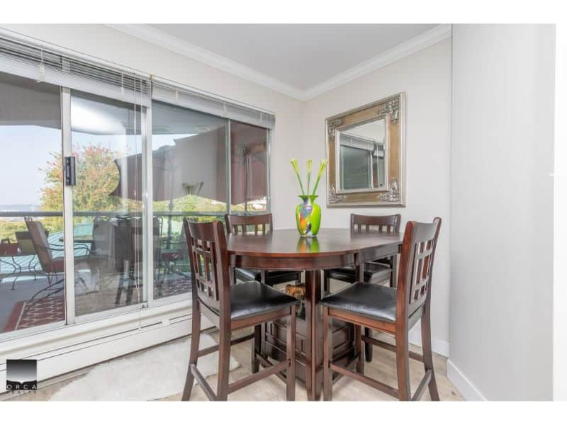 Bright dining area with a wooden table, black leather chairs, large sliding glass door leading to an outdoor balcony, and a decorative mirror on the wall, perfect for family gatherings.