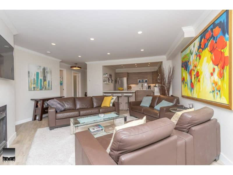Spacious modern living room with leather sofas, colorful artwork, and open-concept kitchen - perfect for Vancouver homes and real estate listings.