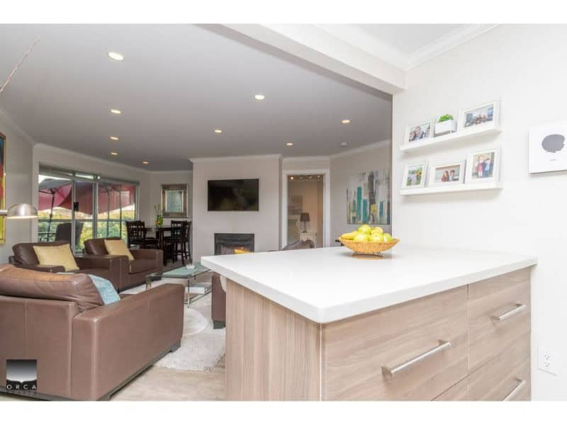 Modern open-concept living room with comfortable seating, flat-screen TV, fireplace, and large windows overlooking a patio in a stylish BC home.