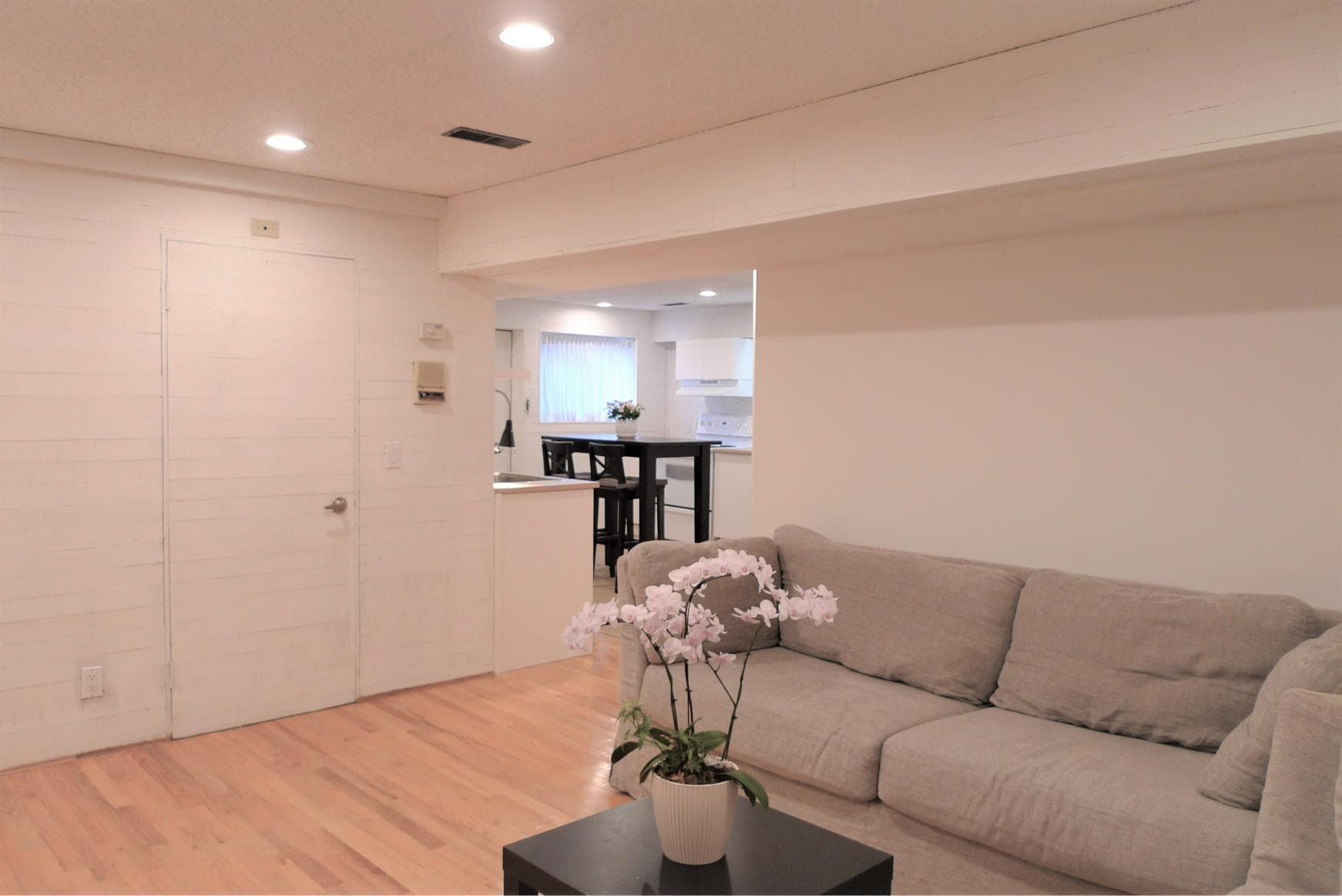 Bright modern living room with neutral tones, hardwood flooring, and stylish decor, seamlessly connected to a well-lit kitchen area, perfect for comfortable Vancouver home living.