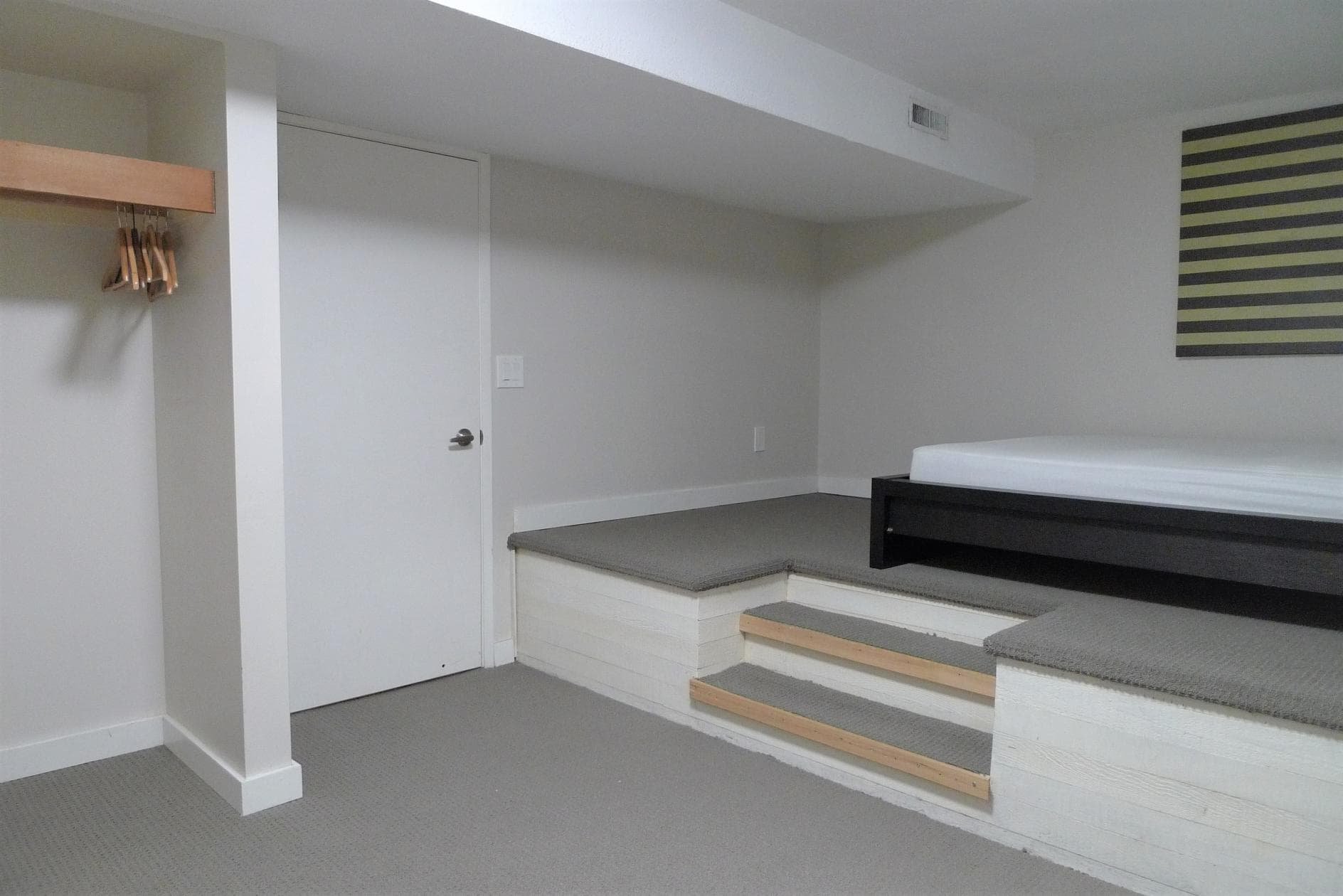 Brightly lit interior of a modern residential unit with a small white door, neutral-colored carpet, and a built-in platform bed with gray carpeting, ideal for Vancouver or BC real estate listings.