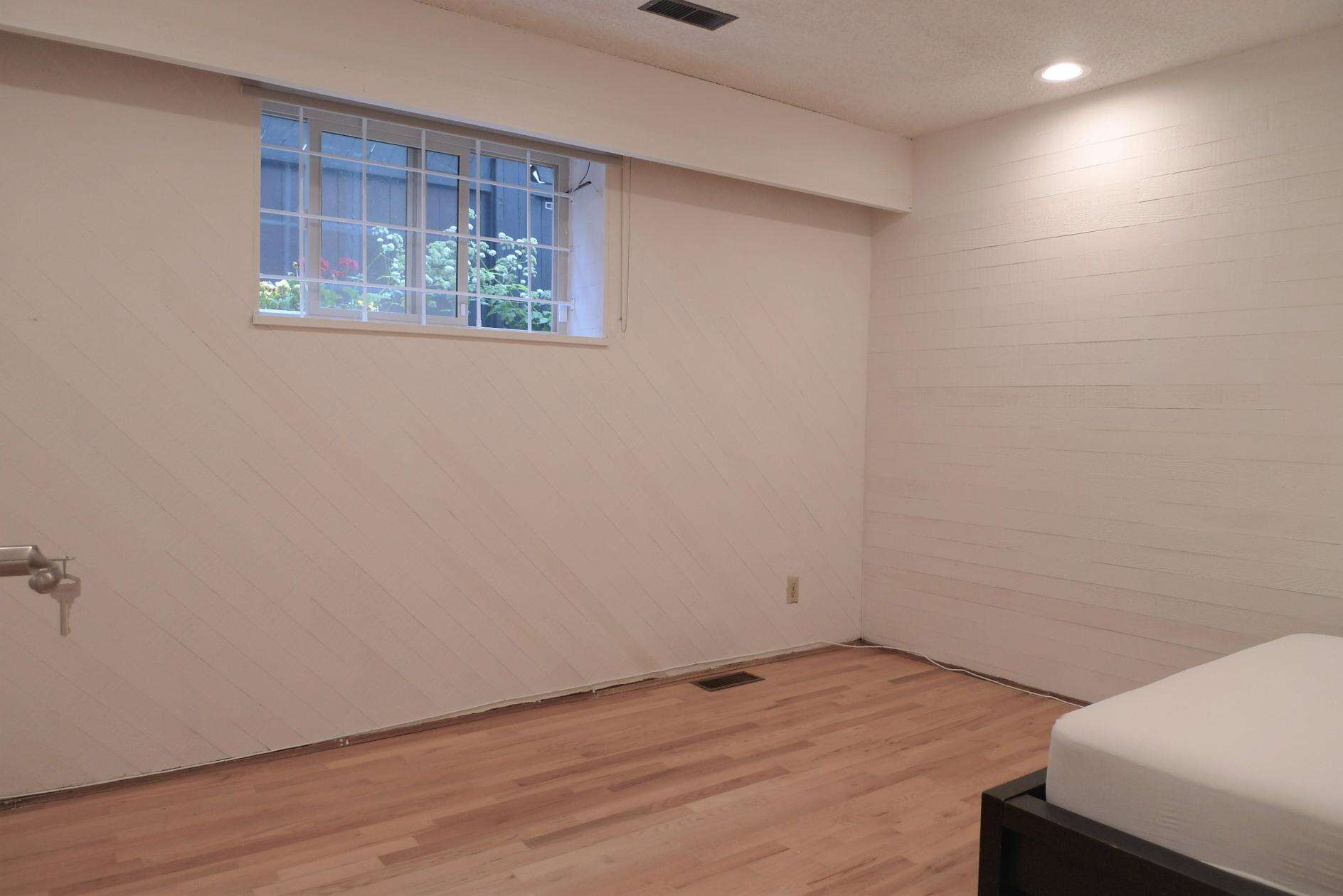 Bright basement bedroom with a window, light coloured walls, and hardwood flooring, perfect for a Vancouver property listing.