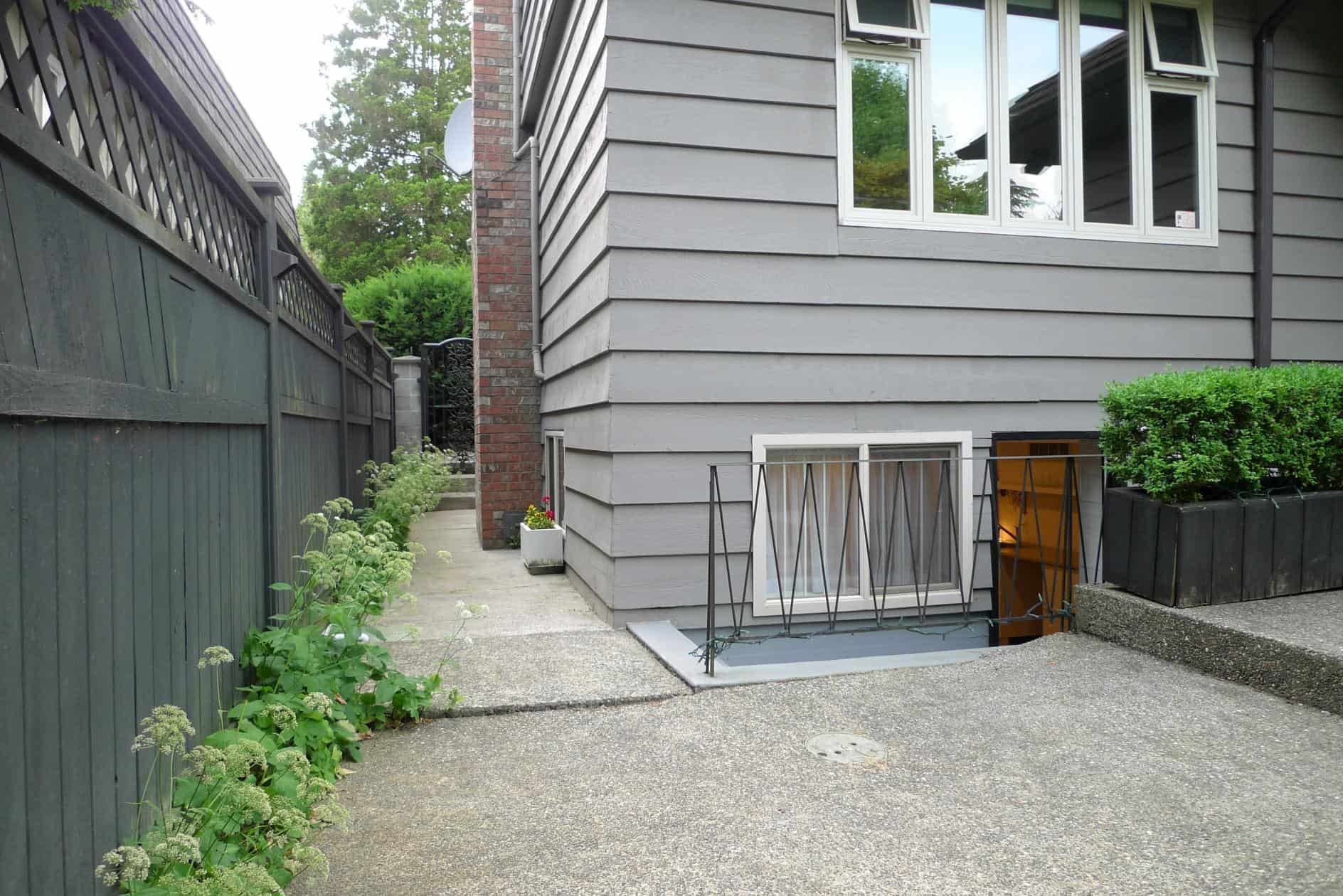Bright and inviting house exterior with accessible basement entry, modern grey siding, well-maintained landscaping, and privacy fencing, showcasing Vancouver real estate offerings by Orca Realty Inc.