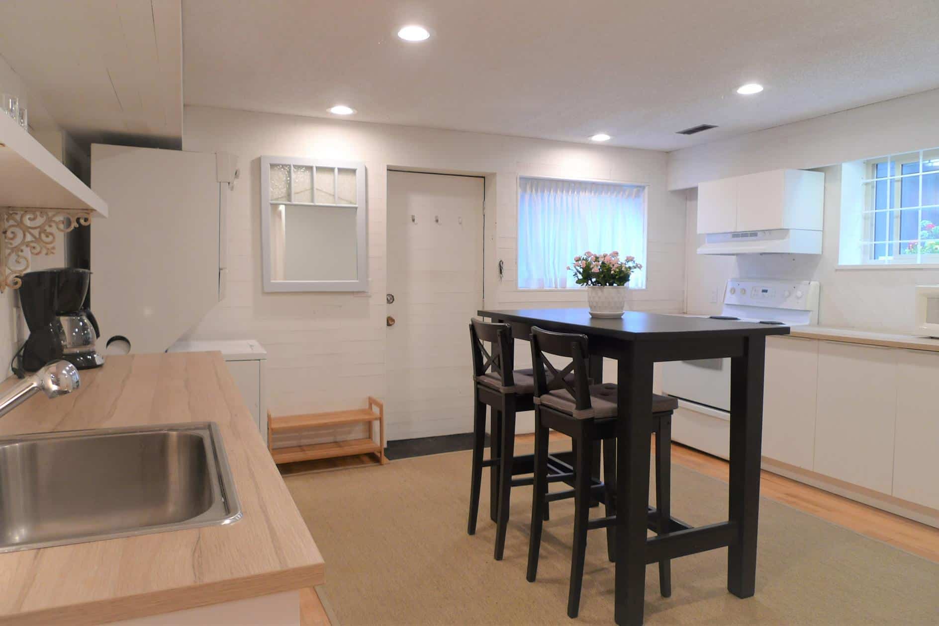 Modern kitchen featuring white cabinetry, a black island with bar stools, stainless steel sink, and natural light from windows, perfect for Vancouver Island real estate.