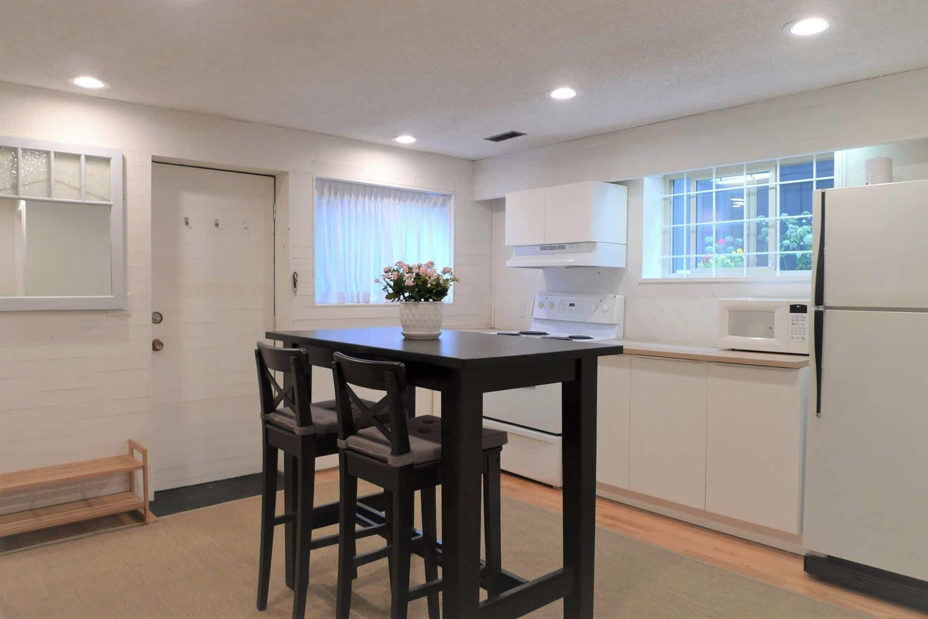 Bright, modern kitchen in a cozy home, featuring white cabinetry, a refrigerator, microwave, and a small dining area with black table and chairs. Perfect for family living and homeownership in Victoria.