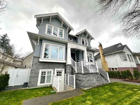 Modern family home with grey siding and stone accents, featuring a welcoming front porch, large windows, and a landscaped lawn in a desirable neighbourhood.