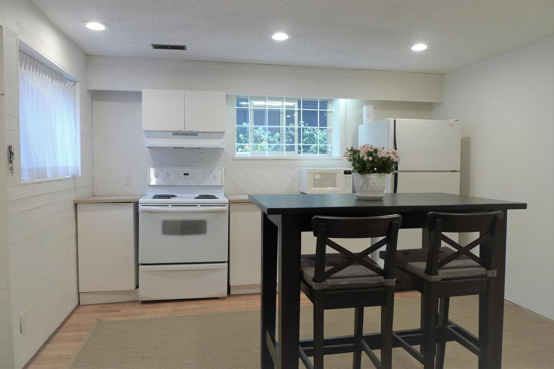 Bright, modern kitchen with white appliances, a black dining table, and a window overlooking a lush garden, perfect for homebuyers seeking a cozy, updated space.