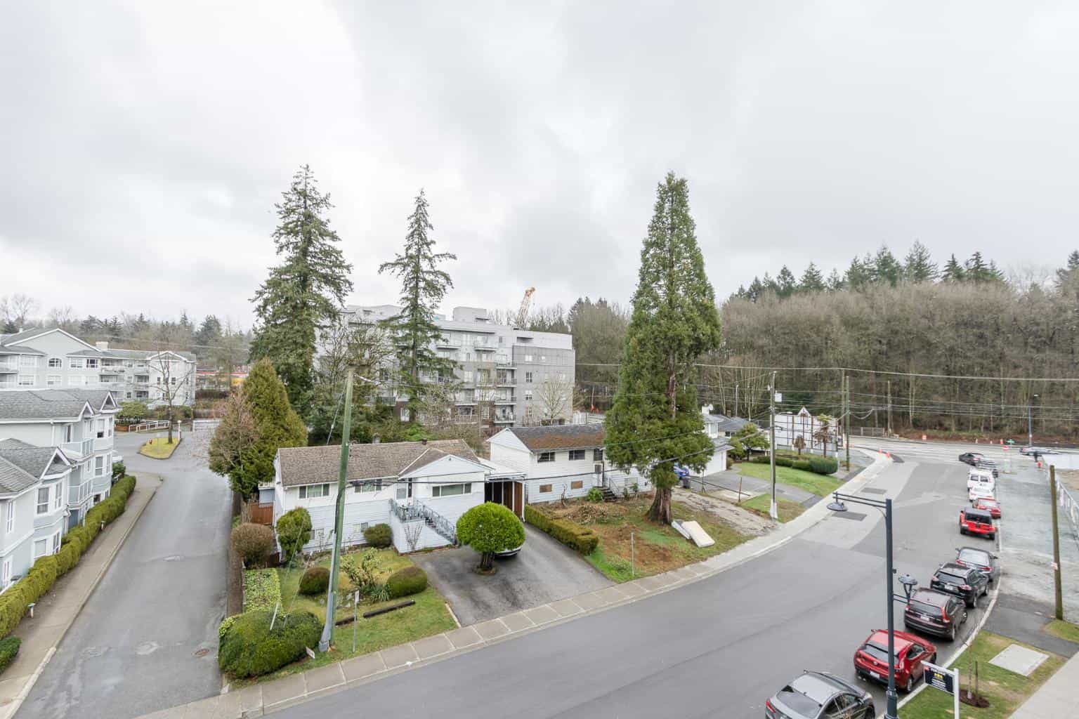 Aerial view of residential neighborhood with houses, trees, and parking lot in court in a Vancouver suburb, featuring lush greenery and multi-unit dwellings.