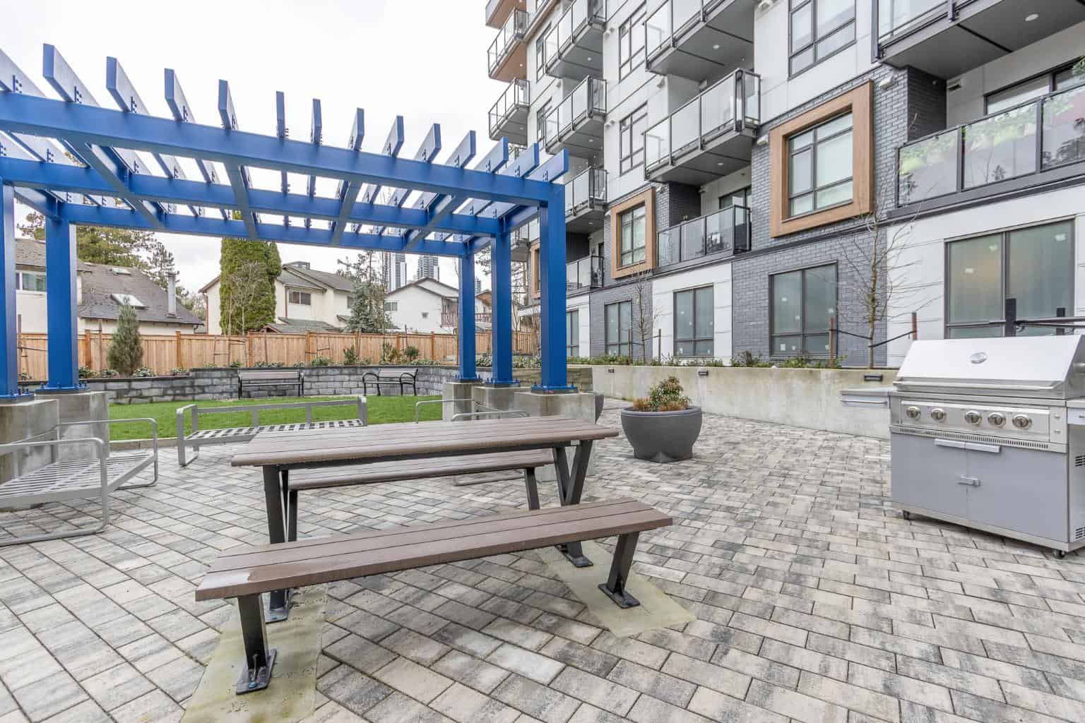 Bright outdoor terrace with modern seating, blue pergola, and BBQ grill at Orca Realty Inc. residential building in Vancouver, BC. Perfect space for social gatherings and outdoor dining.