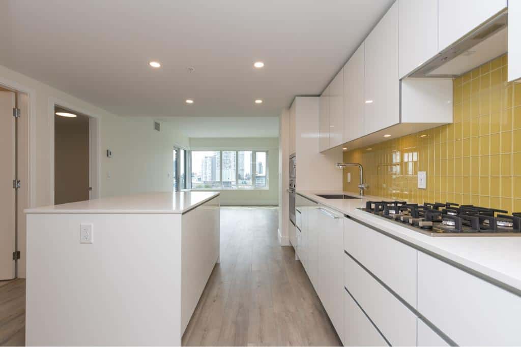 Modern open-concept kitchen with white cabinetry, yellow tiled backsplash, built-in appliances, and ample natural light – ideal for Vancouver real estate.