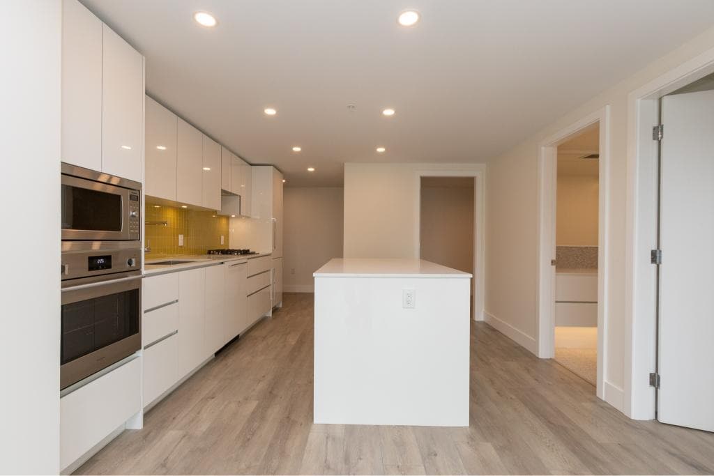 Modern white kitchen with minimalist design, built-in appliances, and ample storage space at Orca Realty Inc.