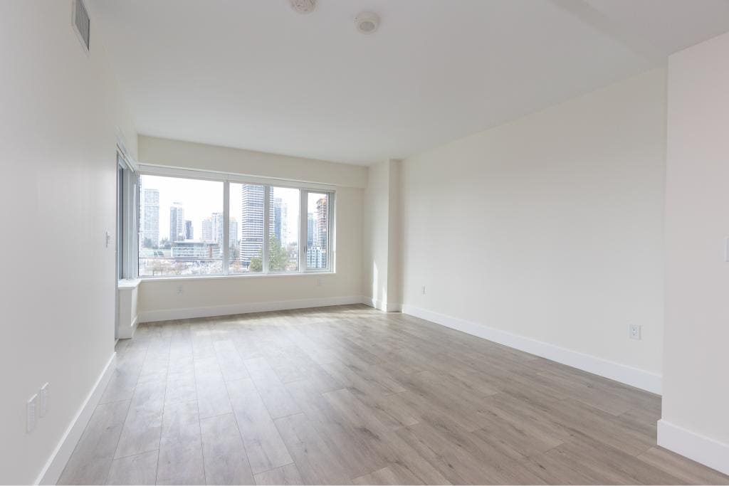 Bright empty living room with large windows showcasing city skyline views, modern flooring, and white walls, perfect for Vancouver real estate or condo listings.