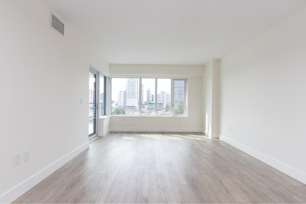 Bright modern living room in a high-rise waterfront condo with large windows overlooking Vancouver skyline, featuring neutral decor, hardwood floors, and ample natural light – ideal for Vancouver real estate buyers.