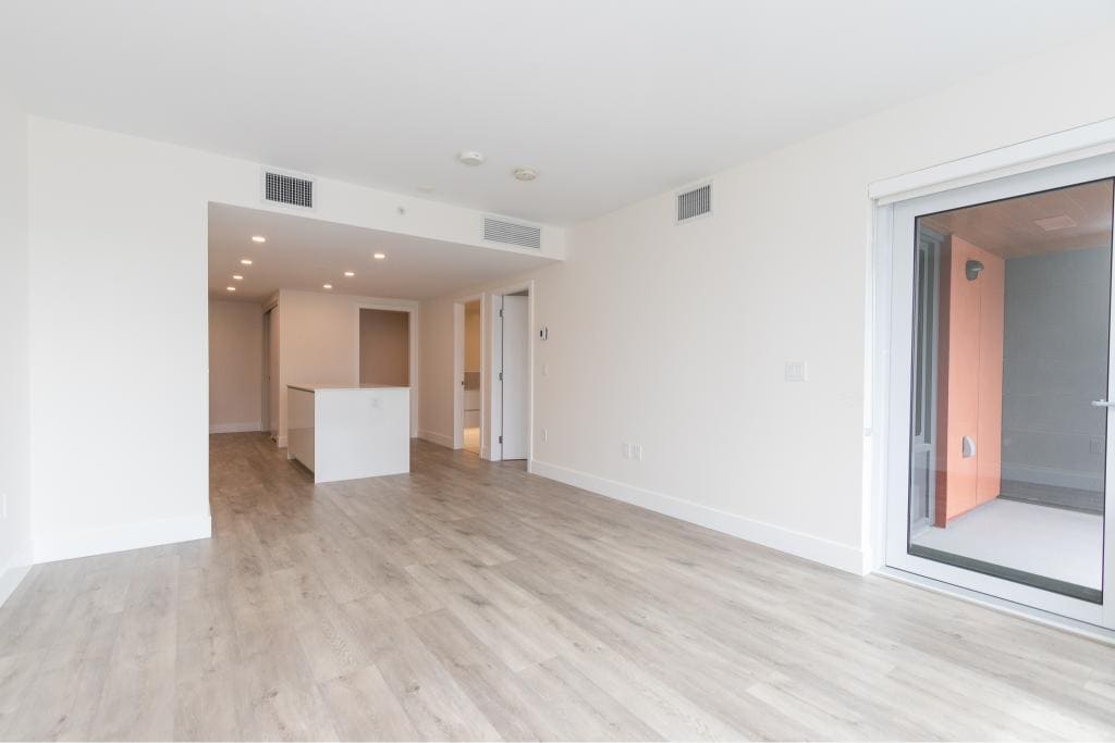 Contemporary open-plan living space in a modern condo with white walls, light wood flooring, and large sliding glass doors leading to a private balcony, perfect for Vancouver real estate buyers.