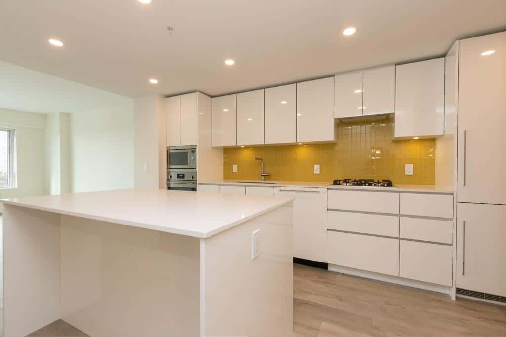 Modern white kitchen with bright yellow backsplash, built-in appliances, and spacious island, ideal for family living and entertaining in Vancouver Island homes.