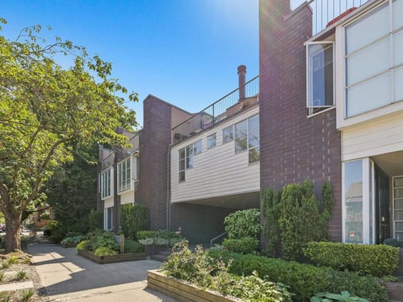 Modern multi-level townhouse with brick and siding exterior, surrounded by lush landscaping and mature trees in a residential neighbourhood in Vancouver, BC.