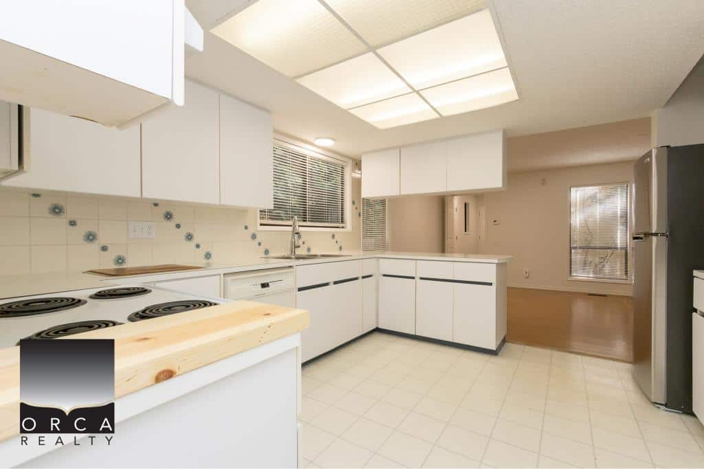 Bright and spacious kitchen in a modern home listed by Orca Realty Inc., featuring white cabinetry, electric stove, and ample natural light, perfect for Vancouver Island real estate buyers.