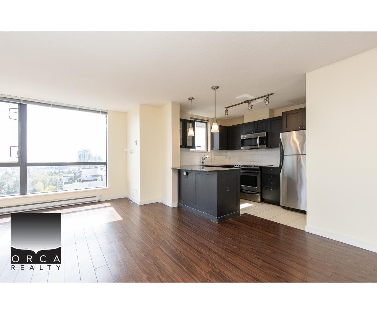 Bright, modern open-concept apartment with kitchen featuring stainless steel appliances and sleek dark cabinetry, large windows providing ample natural light, ideal for Vancouver real estate buyers.