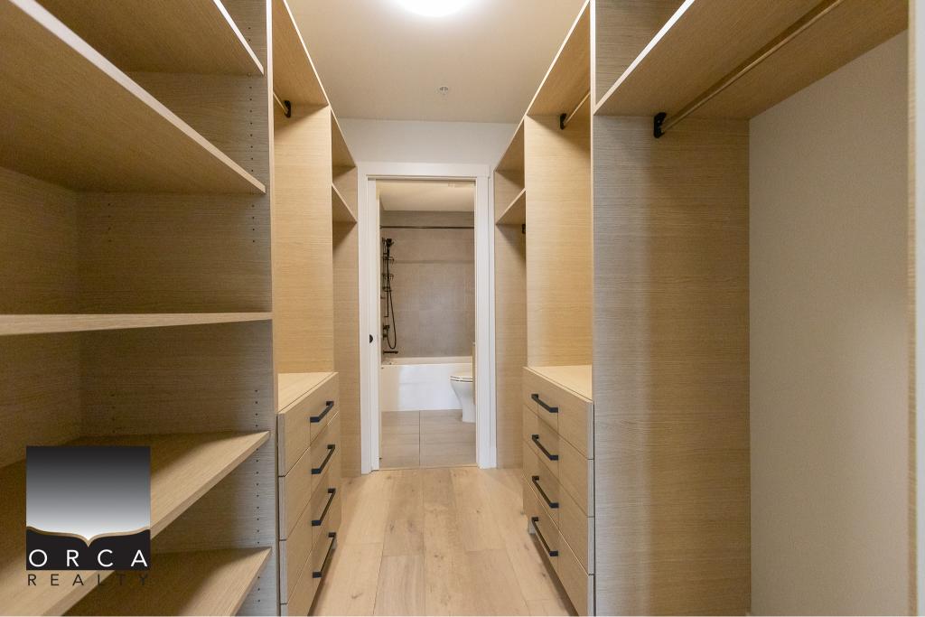 Spacious walk-in closet with custom built-in wooden shelves and drawers, leading to a modern bathroom in a luxury home. Perfect for organizing clothes and accessories.