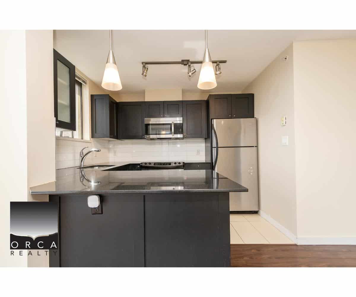 Bright modern kitchen with dark cabinetry, stainless steel appliances, granite countertops, and contemporary pendant lighting, perfect for Vancouver real estate buyers.