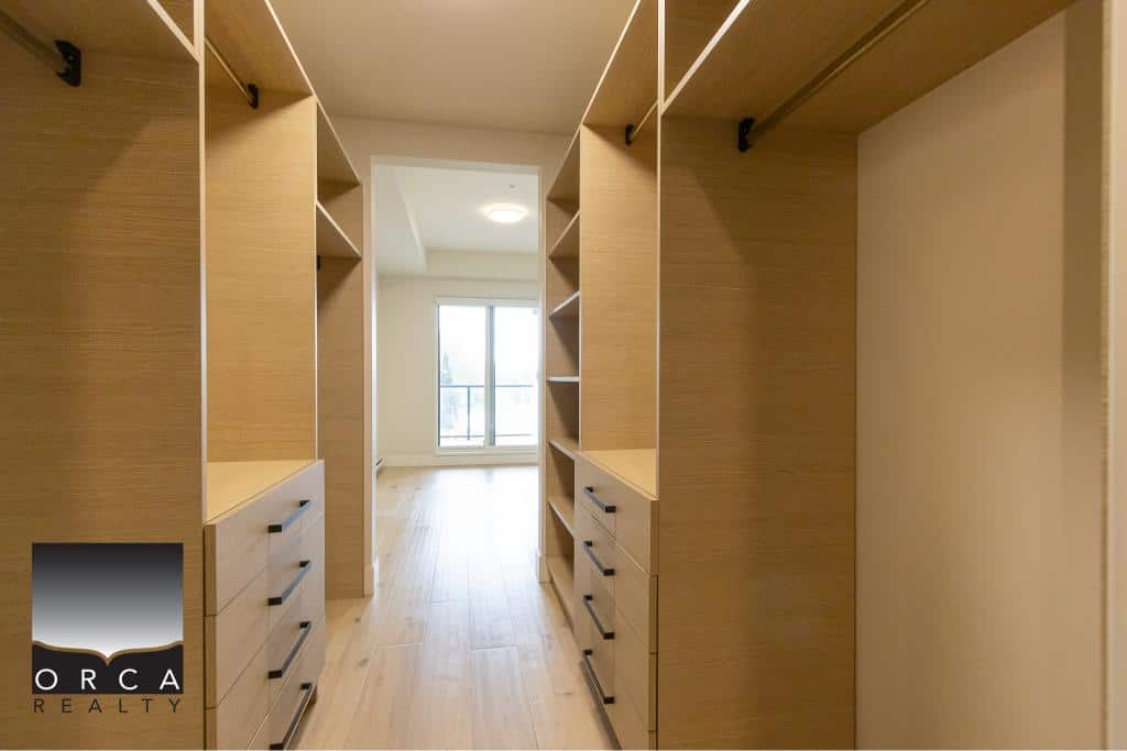 Spacious walk-in closet with custom wooden shelving and storage in a modern apartment. Perfect for organizing clothes and accessories. Bright natural light in the background enhances the space.