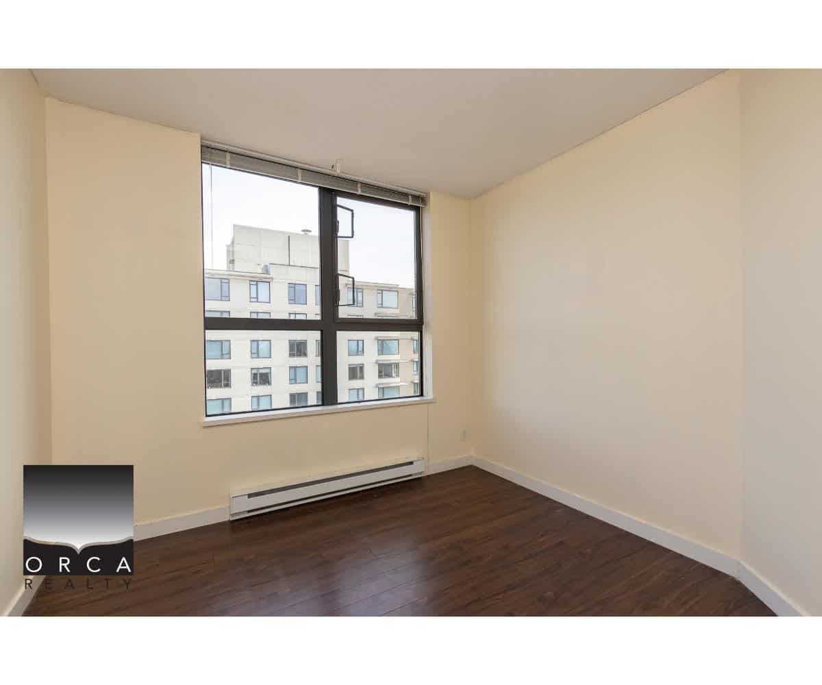 Bright unfurnished apartment room with large window and city view, wooden flooring, and neutral walls, ideal for Vancouver real estate buyers seeking modern rental or purchase options.