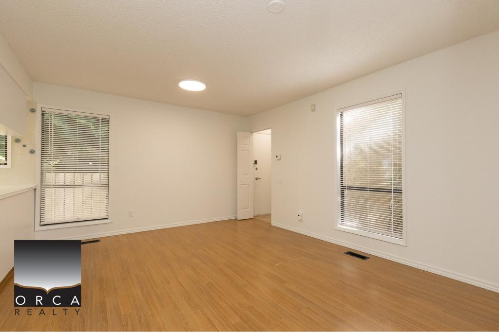 Bright empty living room with large windows, white walls, hardwood flooring, and natural light, ideal for Vancouver Island real estate buyers.