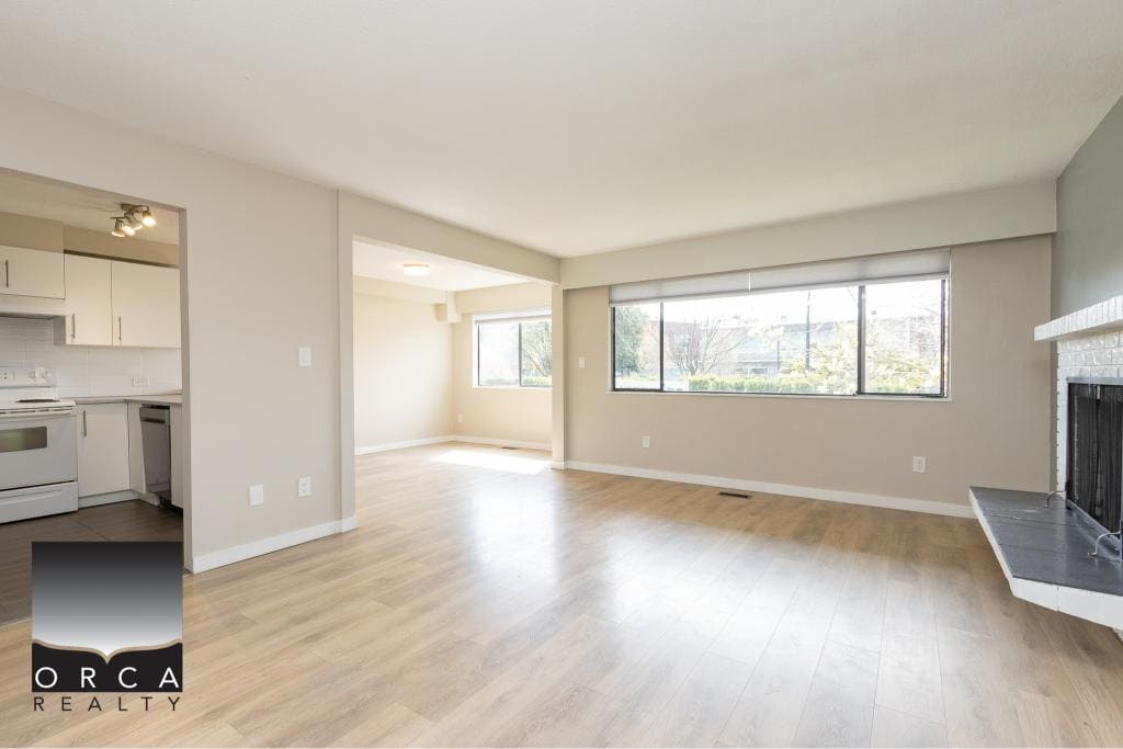 Bright, spacious living room with large windows, hardwood flooring, and a modern fireplace, ideal for buyers seeking a comfortable home in Vancouver Island.
