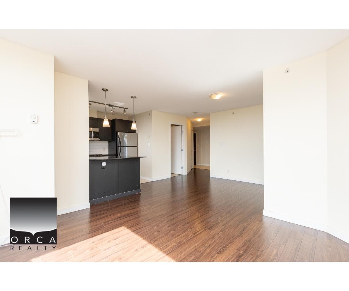 Modern open-concept apartment with hardwood floors, featuring a stylish kitchen with black cabinetry and stainless steel appliances, ideal for Vancouver real estate buyers.