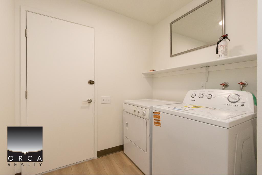 Compact laundry room with washer and dryer, clean white walls, shelf for storage, and fire extinguisher. Ideal for Vancouver and Victoria residents seeking efficient laundry solutions.