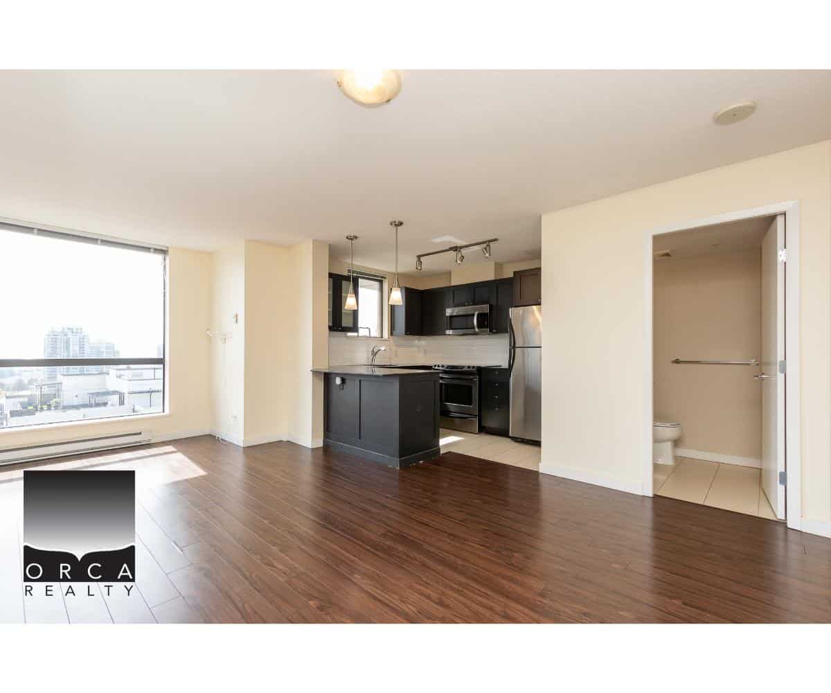 Spacious modern apartment with open-concept living room and kitchen, featuring hardwood floors, stainless steel appliances, large window with city views, and a separate accessible bathroom area.