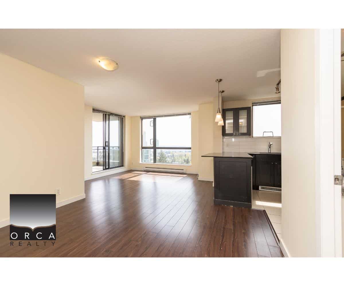 Spacious modern living room and kitchen in downtown Vancouver condo listing by Orca Realty Inc. with large windows, hardwood floors, and contemporary design.