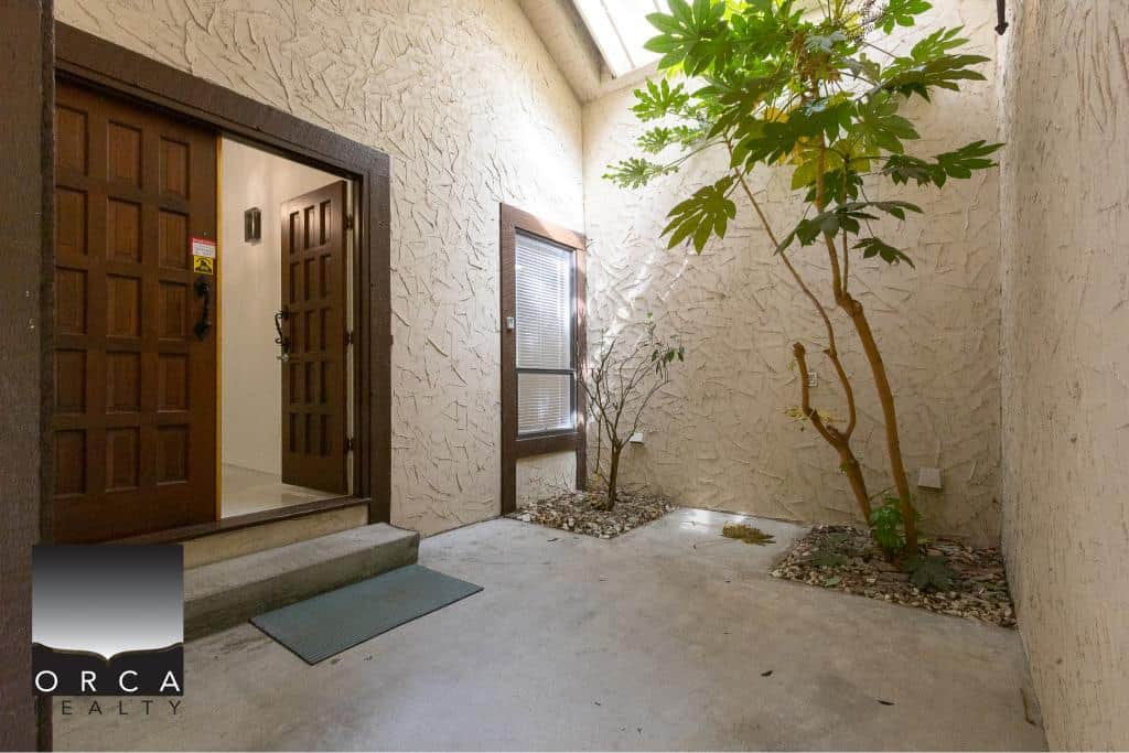 Inviting condo entrance with wooden sliding doors, potted plants, and natural light, showcasing Orca Realty Inc.’s expert real estate services in a beautiful, well-maintained Vancouver area property.