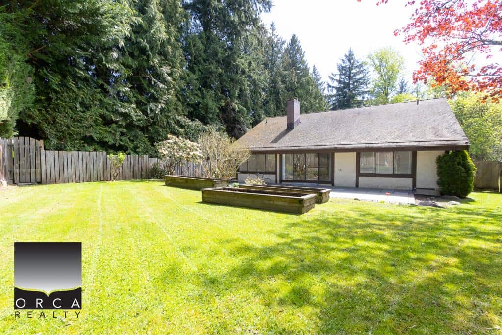 Spacious backyard with lush green lawn, mature trees, and a well-maintained garden at a family-friendly home listed by Orca Realty Inc. in Victoria, BC.