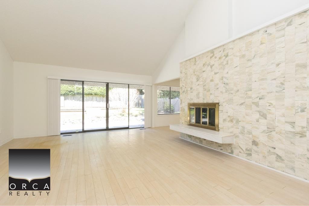 Bright living room with large sliding glass doors, light wood flooring, and a modern fireplace with stone accent wall, ideal for Vancouver Island real estate listings.