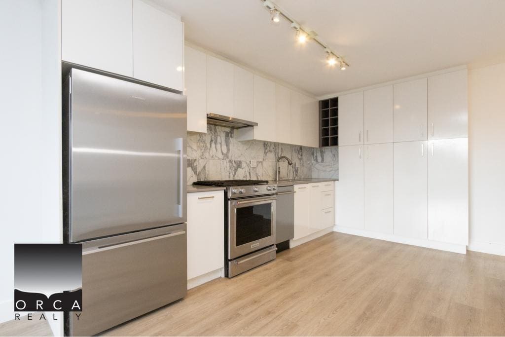 Spacious kitchen in Vancouver condo at 407-231 E Pender St, featuring stainless steel refrigerator, oven, and sleek white cabinets, ideal for contemporary urban living.