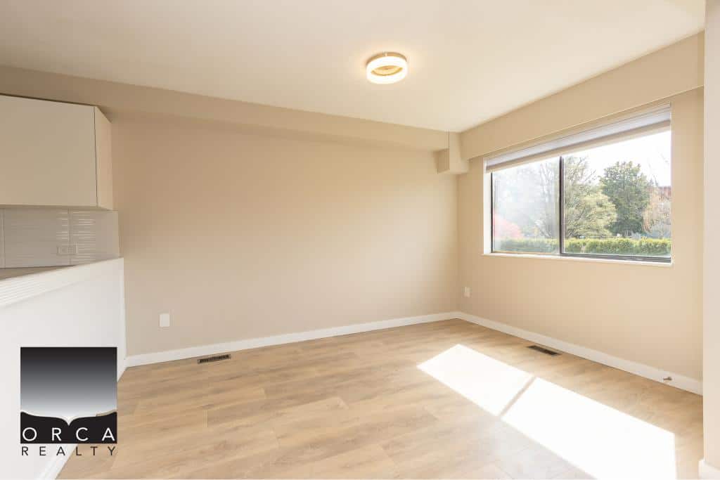 Bright and spacious living room with large window featuring a view of greenery, ideal for family living or entertaining, showcasing modern design by Orca Realty Inc.