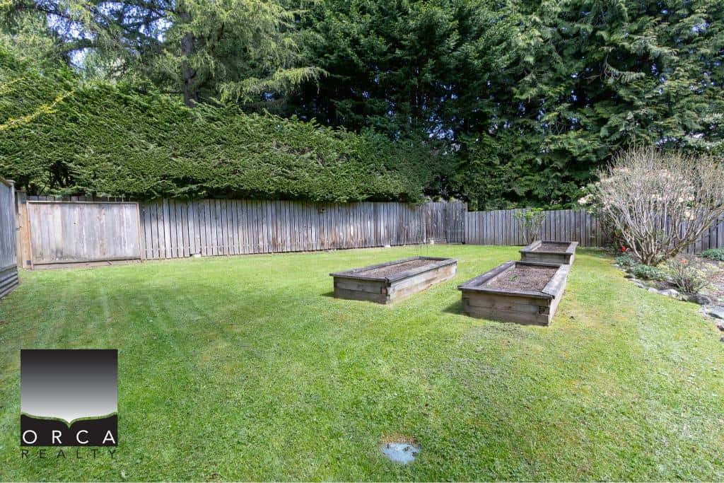 Lush backyard with well-maintained lawn, garden beds, and privacy fence, ideal for outdoor living and gardening in Victoria BC.