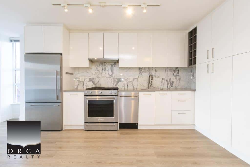 Spacious kitchen in Vancouver featuring sleek white cabinetry, stainless steel appliances, and a marble backsplash, perfect for contemporary living and entertaining.