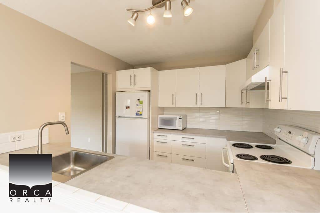 Bright modern kitchen with white cabinetry, electric stove, microwave, refrigerator, and stainless steel sink, ideal for Vancouver Island homes and real estate listings.