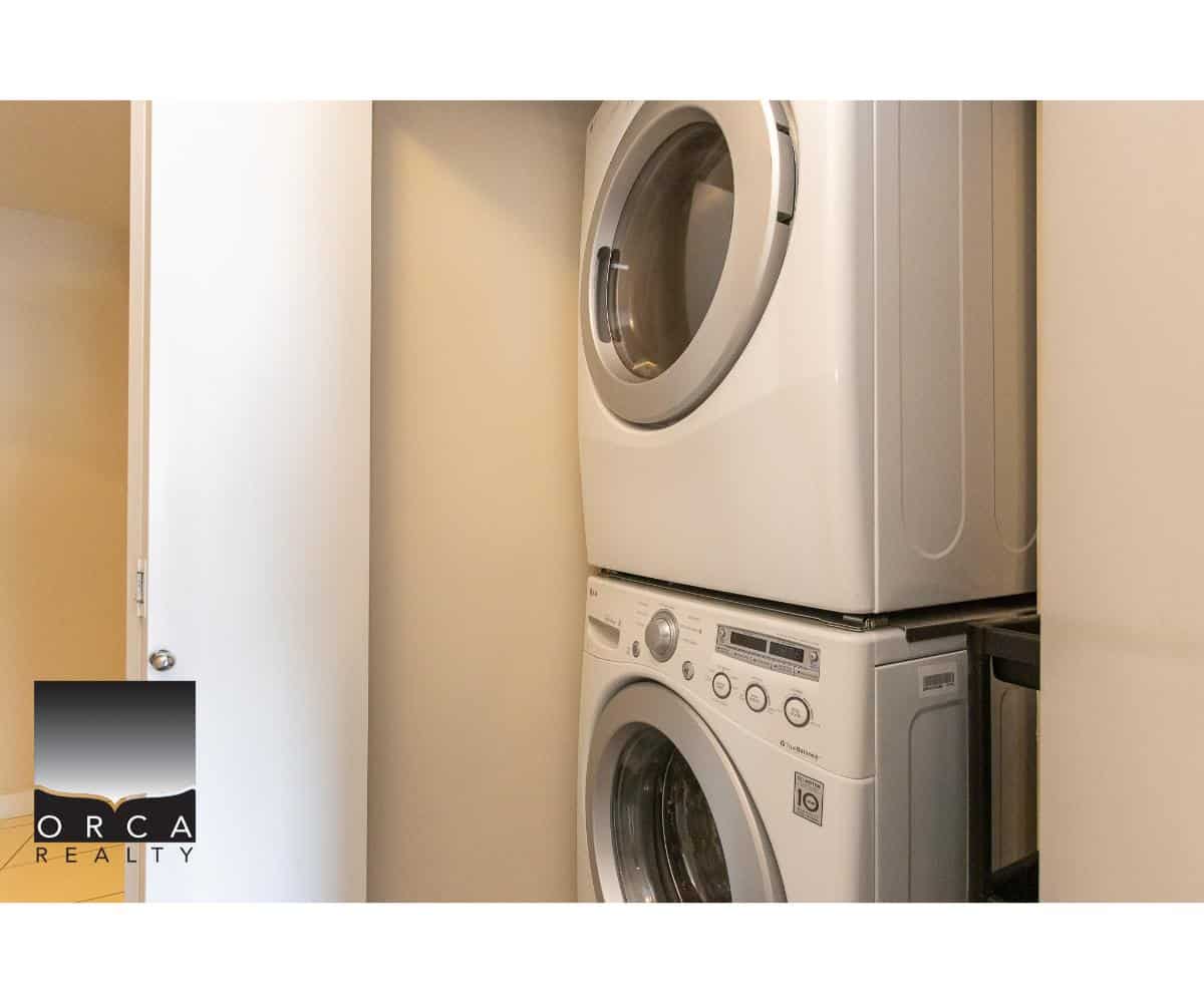 Stacked front-loading washing machine and dryer in a laundry closet, featuring modern appliances, convenient space-saving design, and neutral wall paint for easy home maintenance and efficient laundry routines.